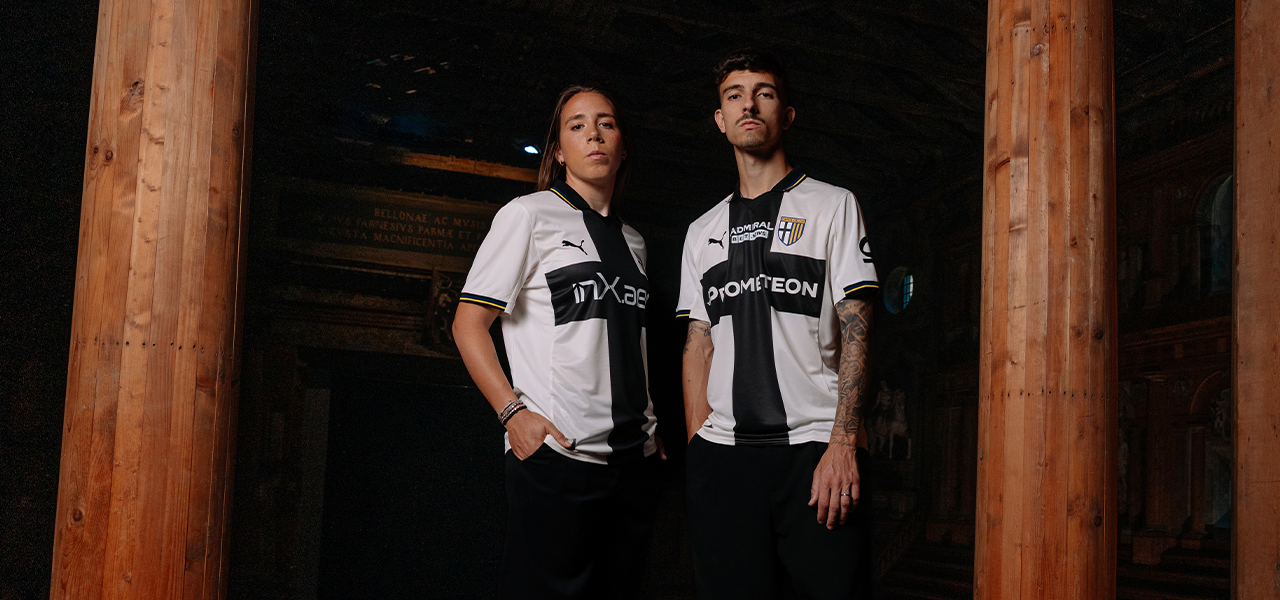 Foto con Ambrosi e Delprato mentre indossano la nuova maglia Home Parma Calcio 2025/26 bianca con croce nera e dettaglio righe gialloblu su colletto e maniche