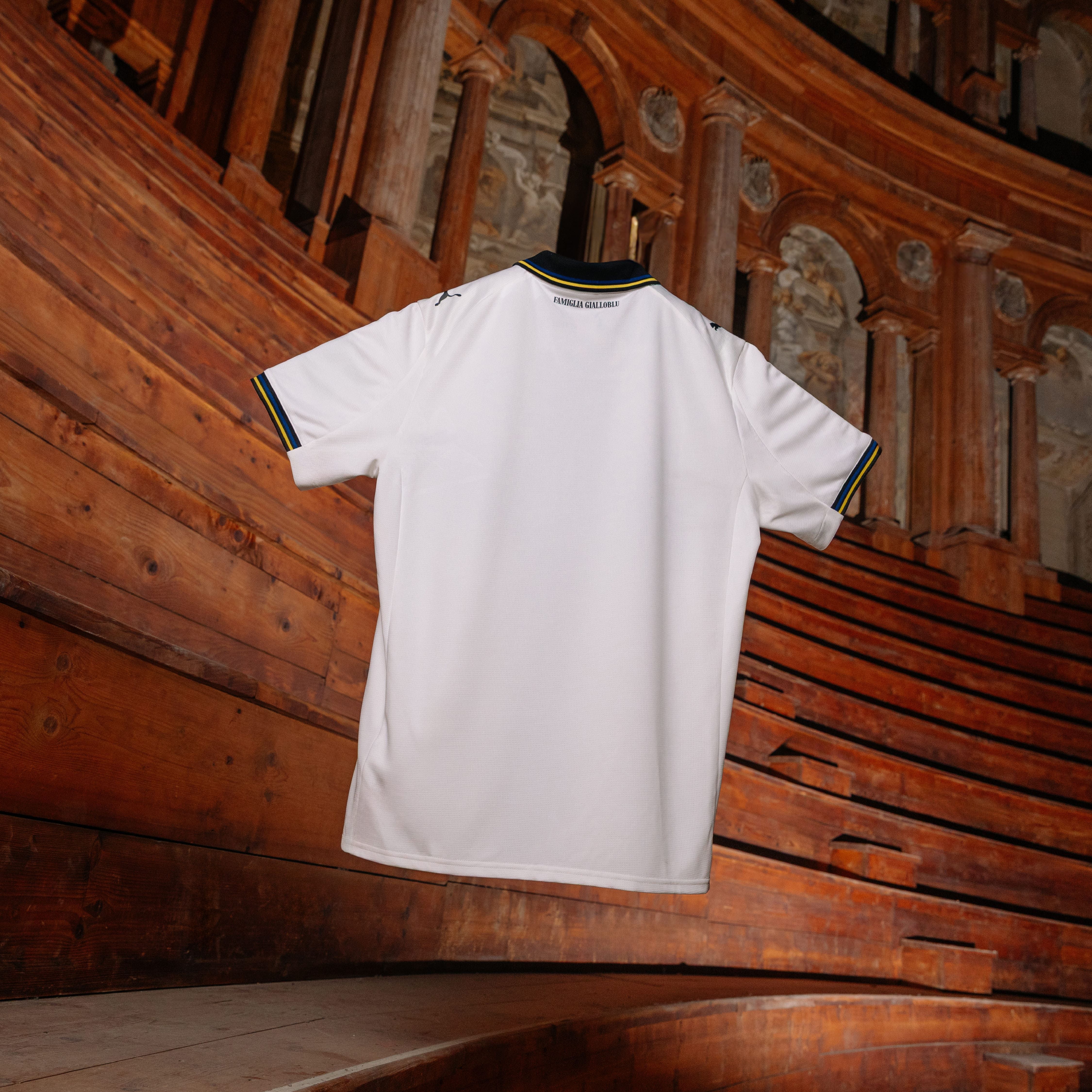 Retro maglia gara Home Parma Calcio bianca con croce nera e dettagli a righe gialloblu su colletto e maniche sospesa in aria con fondo teatro Farnese