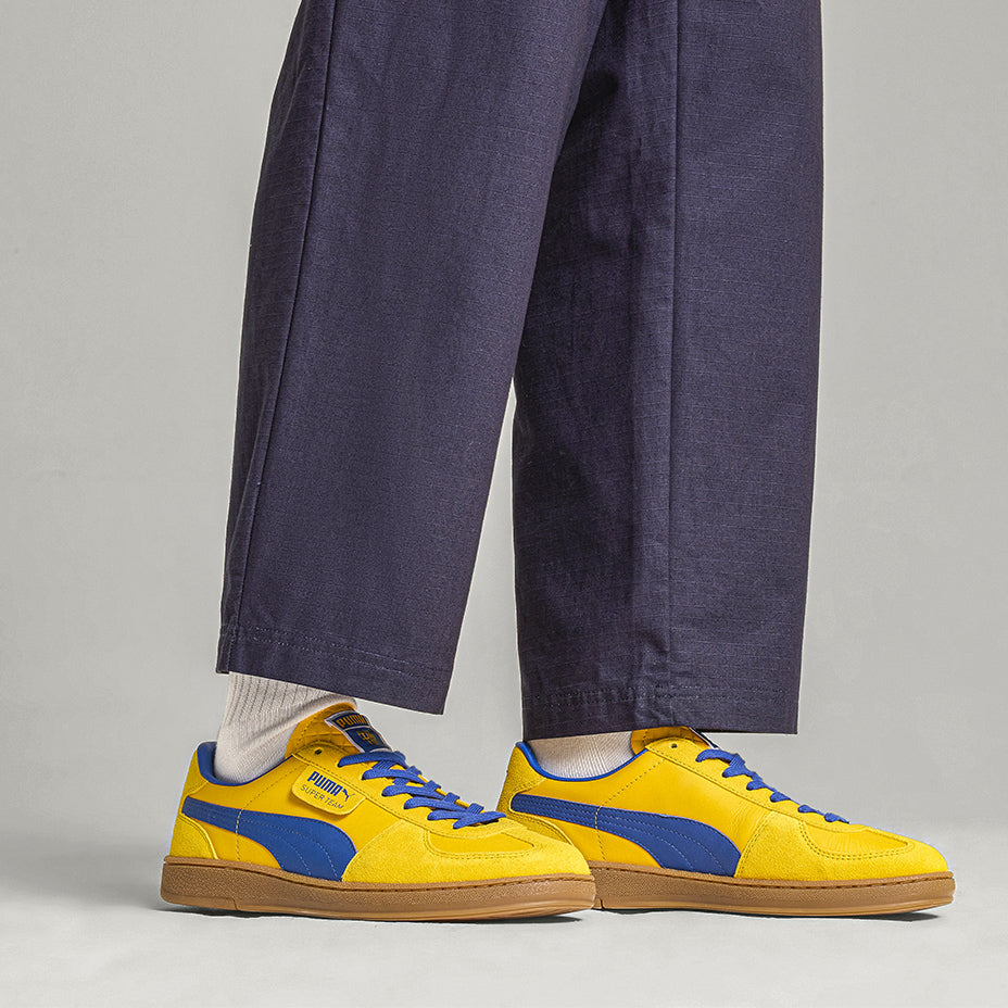 Sneakers puma x parma calcio caratterizzata dal signature tag sulla tomaia in pelle con sovrapposizioni in suede, dalla costruzione T-toe e dalla classica suola gum. Sneakers in colore faster yellow e blu Navy indossate da modello