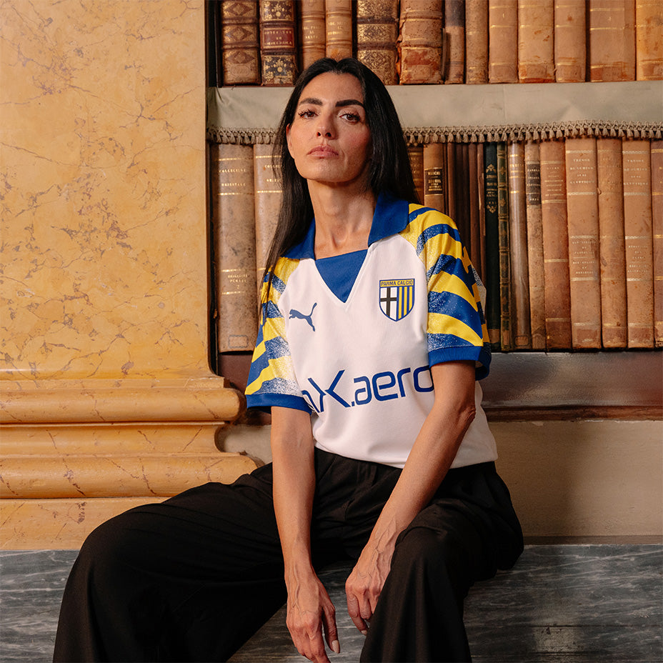 Modella seduta su libreria della biblioteca Palatina con nuova terza maglia gara femminile Parma Calcio bianca con maniche e colletto giallo-blu