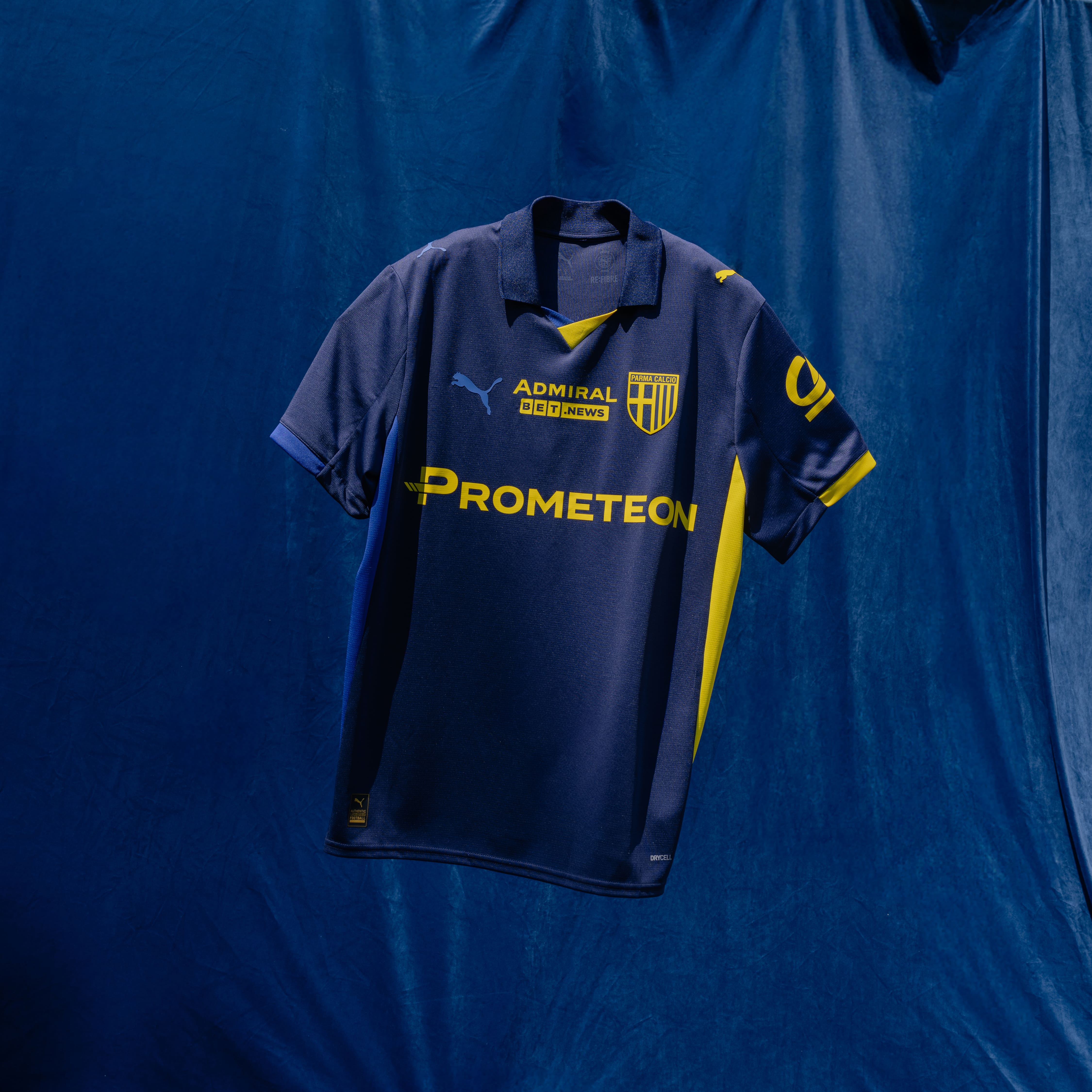 Foto maglia gara Fourth con sponsor gialli prima squadra Maschile. Maglia blu navy con colletto, dettagli laterali e dettagli maniche blu e gialli.